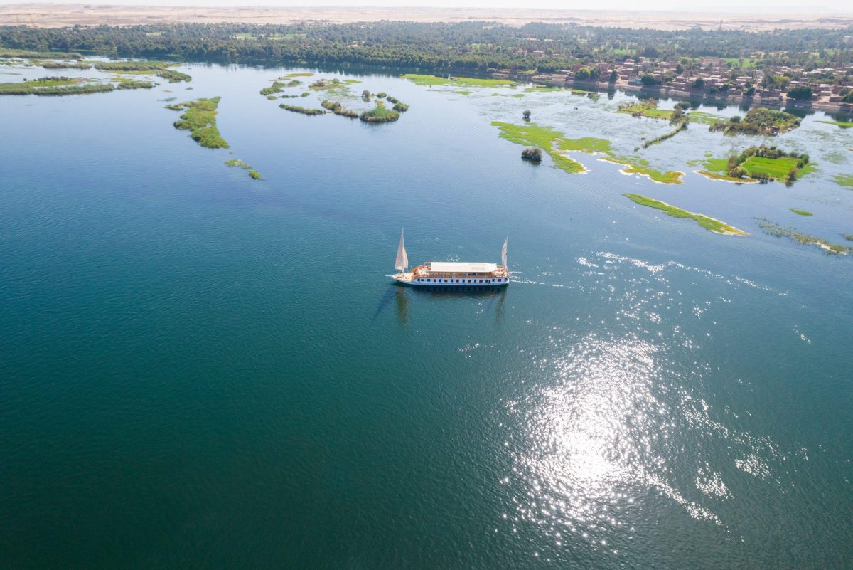 A breathtaking view of the Great Pyramids of Giza and a luxury Dahabiya boat on the river, showcasing why travelers choose to visit Egypt for history, adventure, and premium Nile cruises.