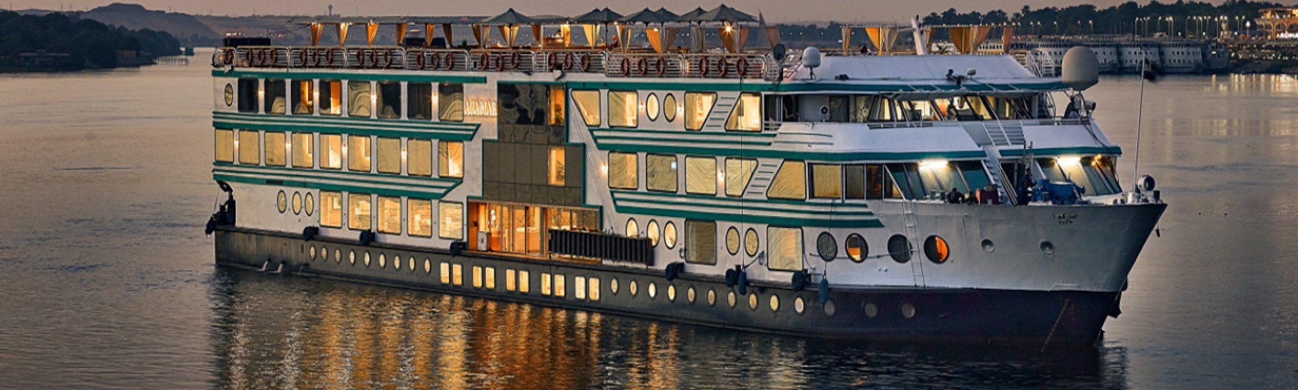 A 5-star Nile Cruise boat sailing past green palm trees and ancient ruins between Luxor and Aswan.