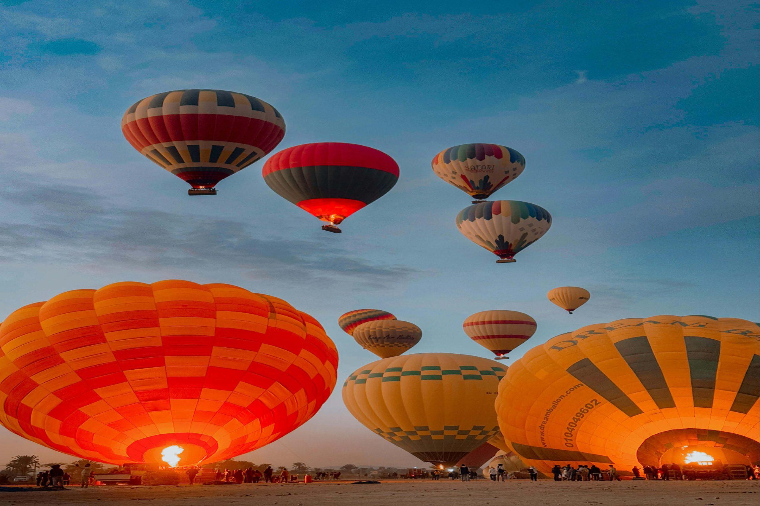 Hot air balloon flying over Luxor at sunrise with Nile River and temples in view