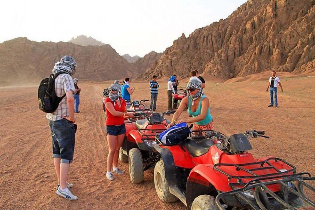 A group on a Hurghada desert safari riding quad bikes across golden dunes at sunset.