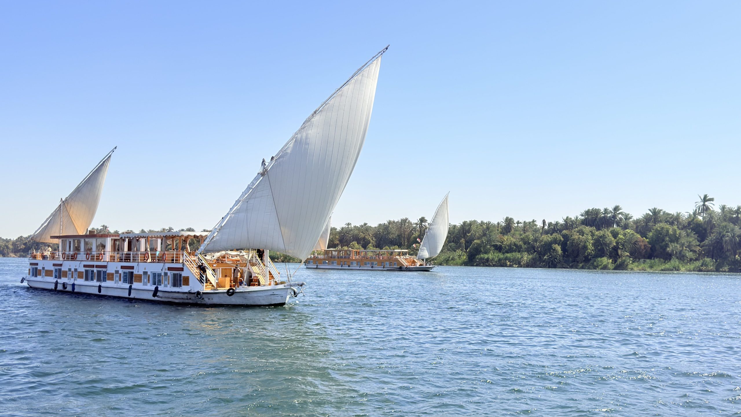 Luxury Dahabiya sailboat cruising the Nile near ancient Egyptian temples with golden sunset.