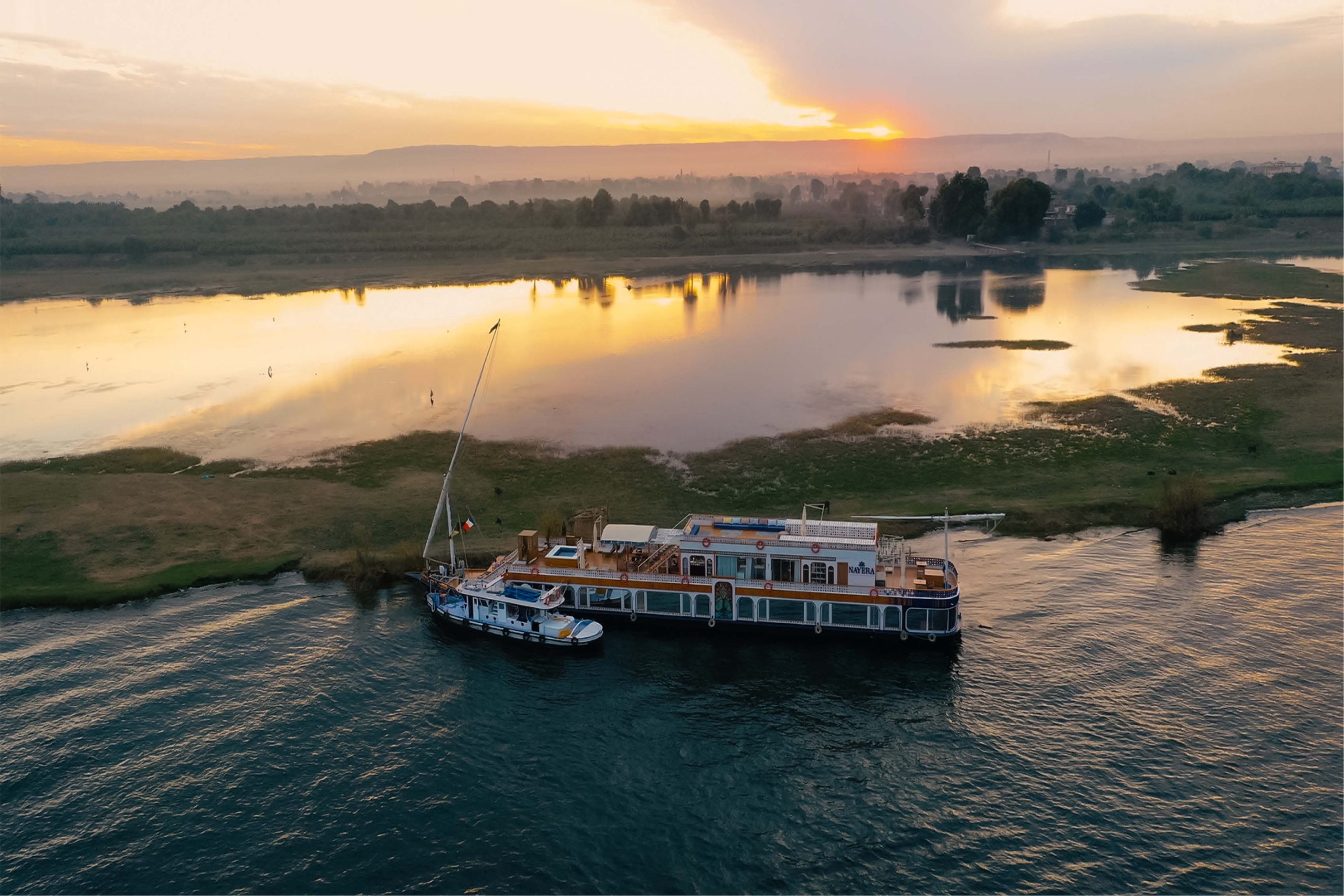 Dahabiya sailing on the Nile at sunset with Luxor temples in the background