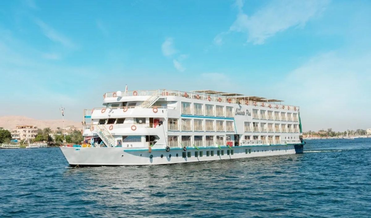 A luxury Nile cruise ship sailing on the river at sunset near an ancient Egyptian temple in Luxor.