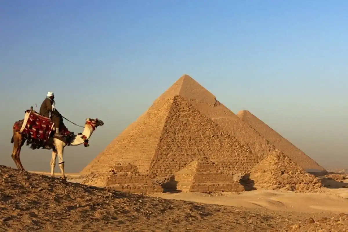 A group of travelers on a camel trek near the Great Pyramids of Giza during a sunset Egypt adventure tour.