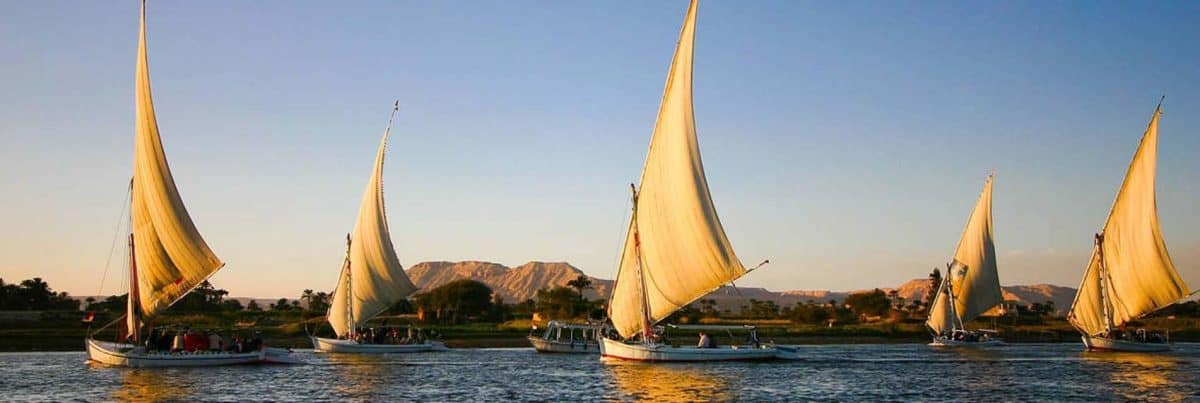 Traditional Egyptian felucca sailing on the Nile river at sunset in Aswan, Egypt.