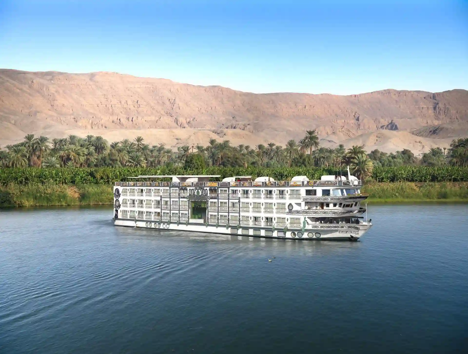 A luxury five-star Nile cruise ship sailing past the palm-fringed banks and desert landscapes of the Nile River in Egypt.