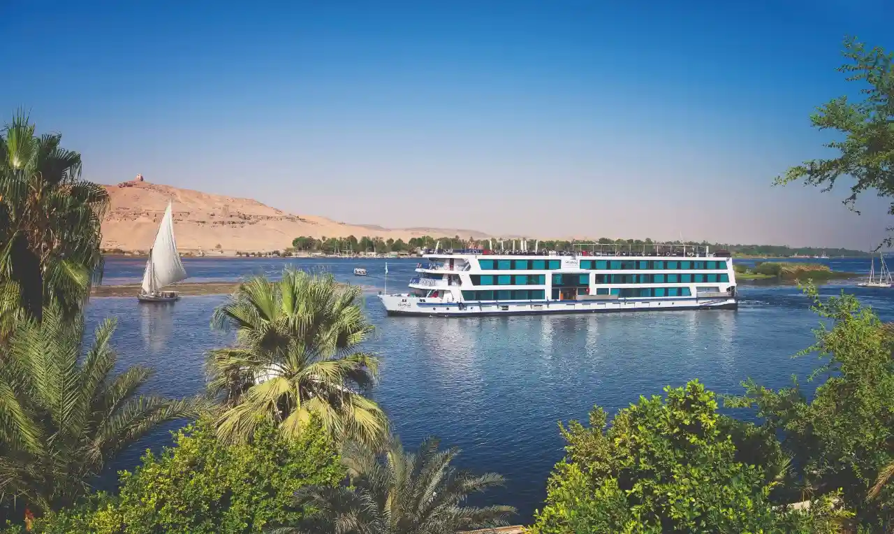 The interior lounge and sun deck of a luxury Nile cruise boat sailing past palm trees in Egypt.