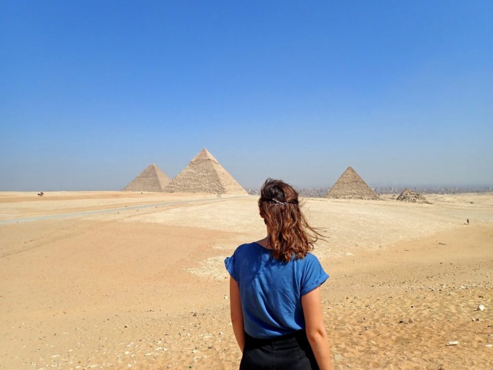 Solo female traveler standing safely near ancient Egyptian monuments during sunset.