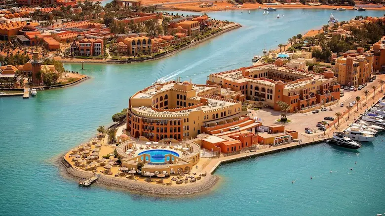 Luxury beachfront resort pool complex in Egypt with palm trees and sun loungers under a blue sky