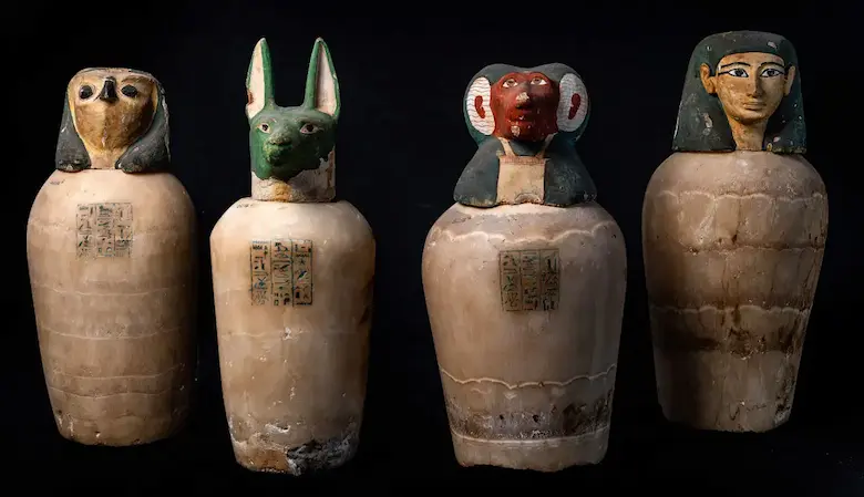 Four ancient Egyptian canopic jars with lids shaped like the Four Sons of Horus: falcon, jackal, baboon, and human heads.
