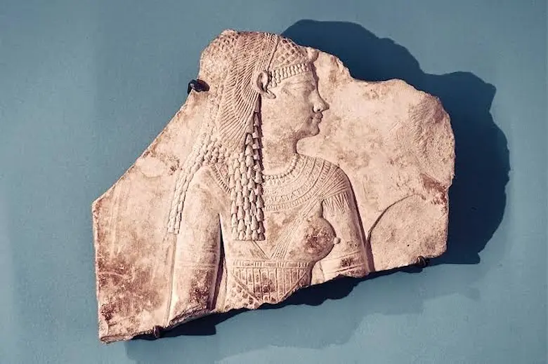Ancient Egyptian relief fragment depicting a Ptolemaic queen, likely Cleopatra VII, shown in profile wearing traditional pharaonic headdress and jewelry.
