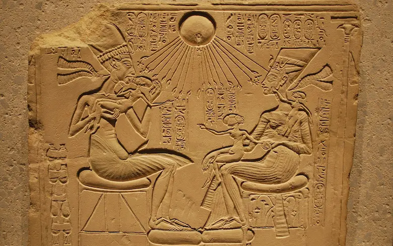Ancient Egyptian limestone stela depicting Pharaoh Akhenaten, Queen Nefertiti, and their daughters sitting beneath the rays of the sun god Aten.