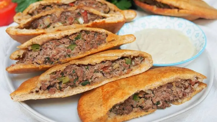 Golden-brown baked Egyptian Hawawshi flatbread cut into quarters, showing a savory spiced minced beef filling inside.