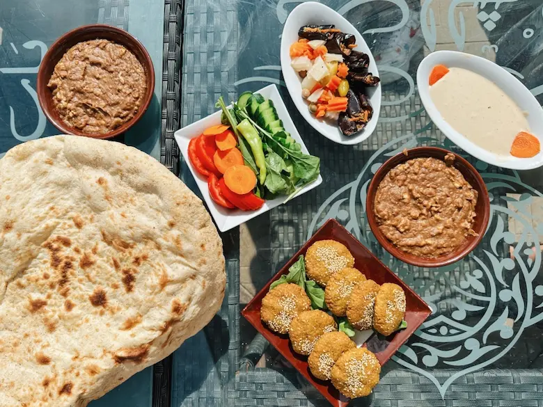 An Egyptian vegan food spread featuring bowls of Koshari, fresh Ta'ameya falafel, Ful Medames, tahini dip, and warm pita bread.